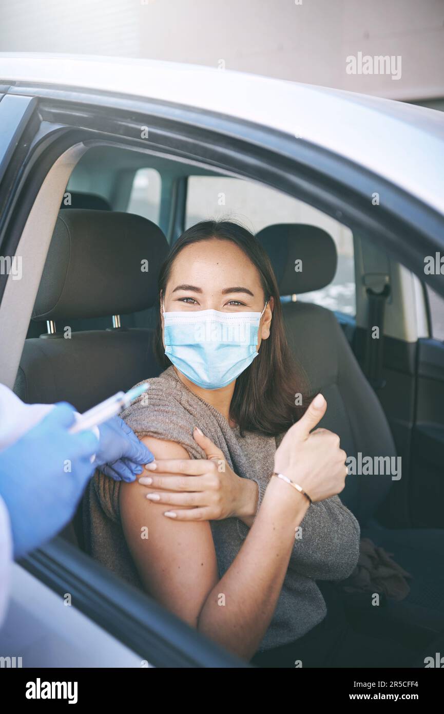 Dire no al virus e sì al vaccino. Una giovane donna mascherata che riceve un'iniezione in un drive Covid-19 attraverso il centro di test. Foto Stock