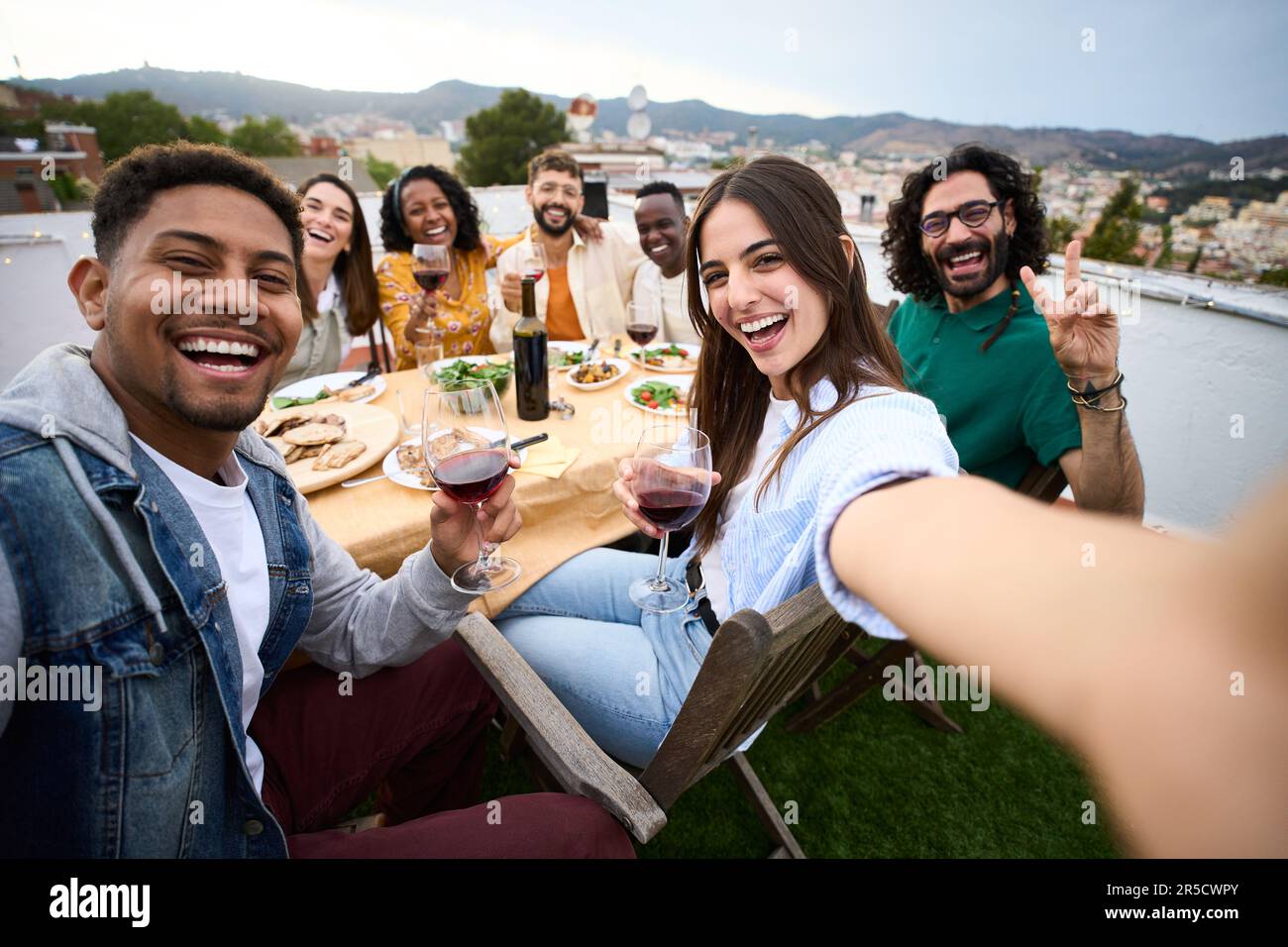 Gruppi diversi amici che si divertono al party sul tetto. Bella donna che prende selfie al momento del barbecue. Foto Stock