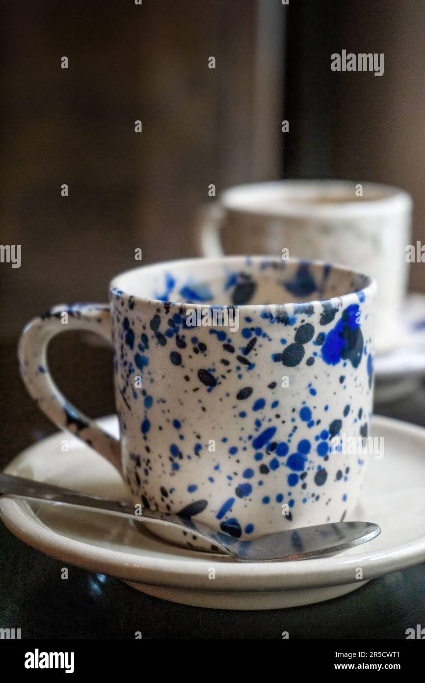 Tazza da caffè bianca con macchie blu su un piattino con un cucchiaio su un tavolo di legno da vicino Foto Stock