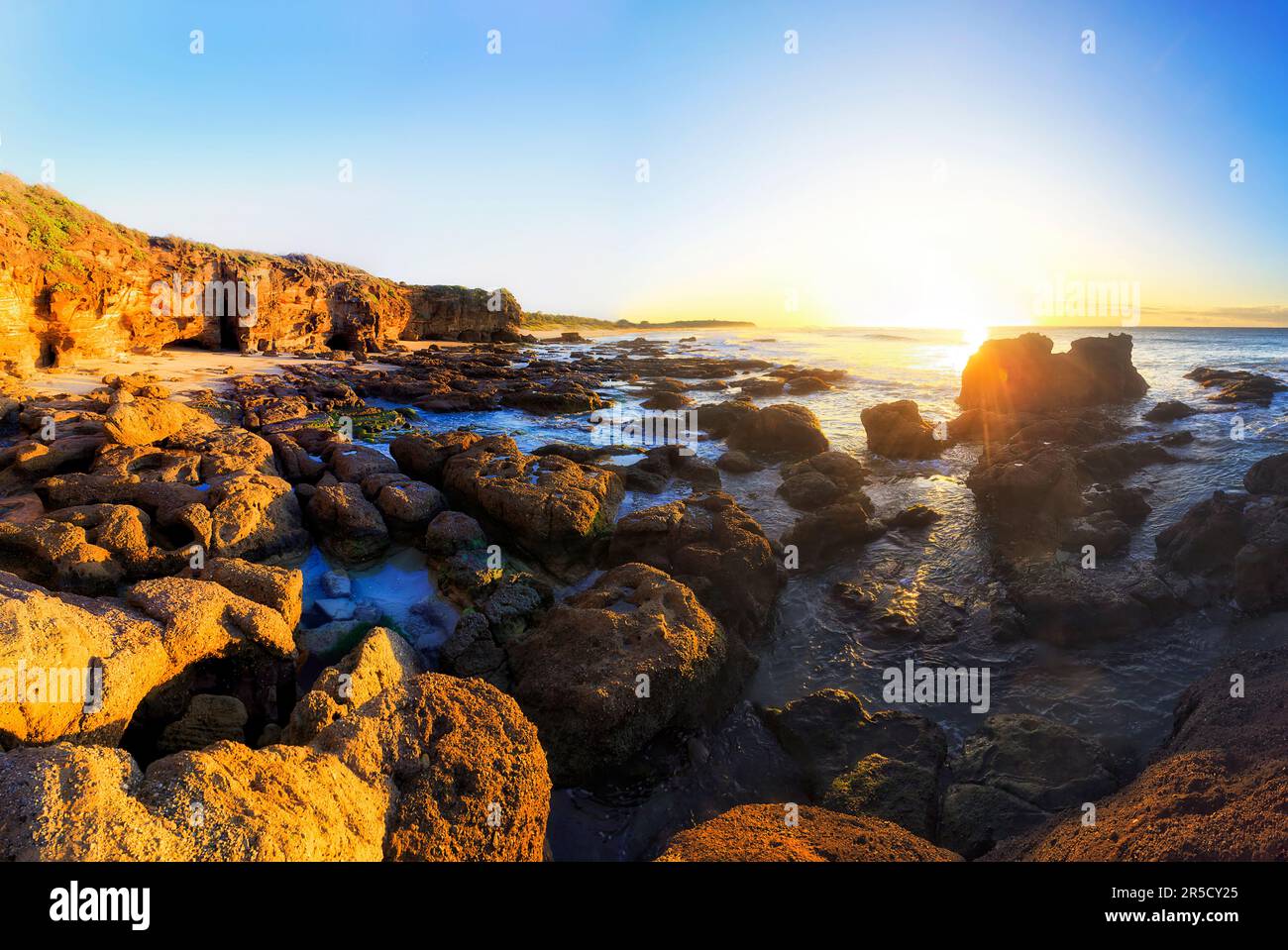 Rocce di massi di arenaria sulla spiaggia di Caves dell'oceano Pacifico in Australia all'alba. Foto Stock