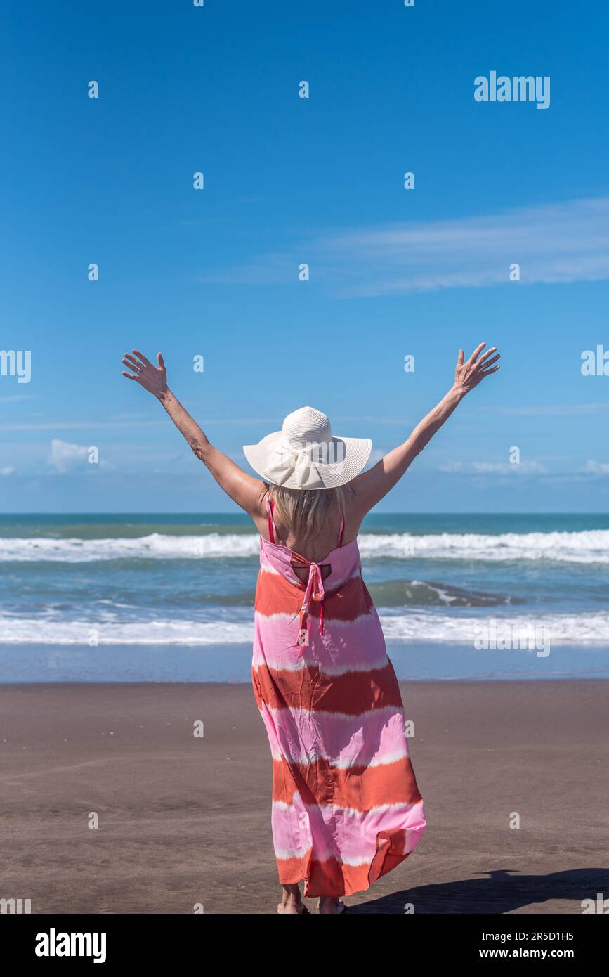 Donna che alza le mani mentre si gode una giornata di sole in spiaggia. Foto Stock