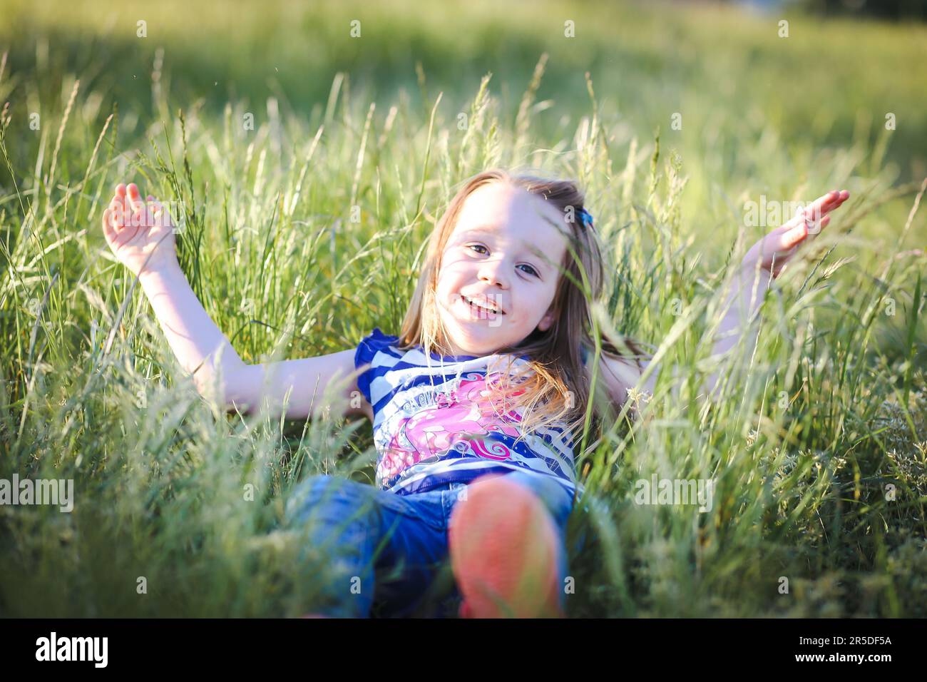 Ragazza piccola felice sdraiata in erba lunga al parco. Divertimento all'aperto nella natura Foto Stock