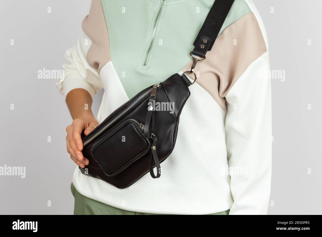 Primo piano Foto della borsa a banana in vera pelle nera con tasca con zip che indossa la tracolla sul modello femminile su sfondo grigio Foto Stock