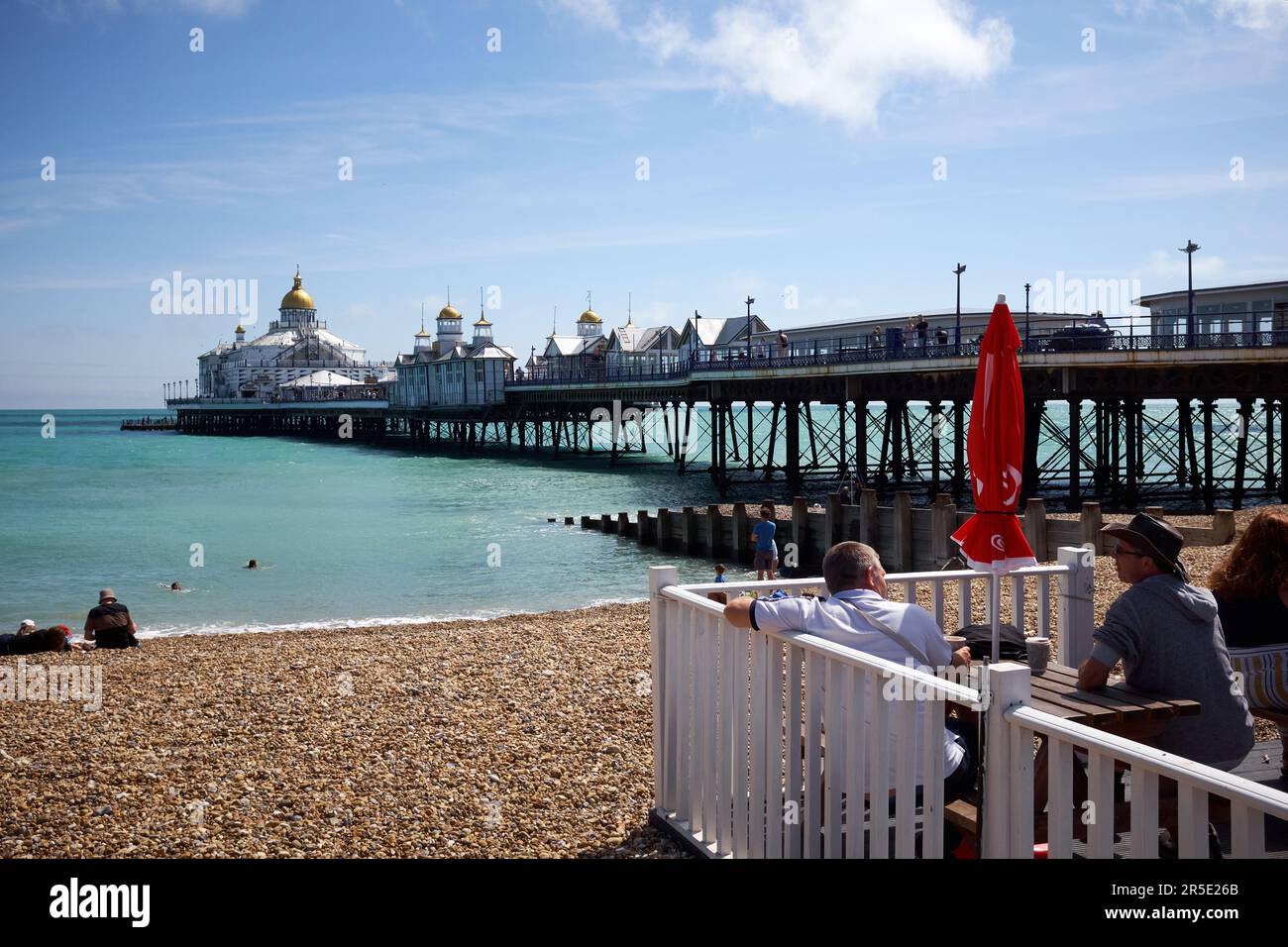 Eastbourne, East Sussex, Regno Unito - 10 2021 agosto: Turisti in un caffè che si affaccia su un ponte in una giornata di sole che si affaccia sul mare con molo sullo sfondo. Foto Stock