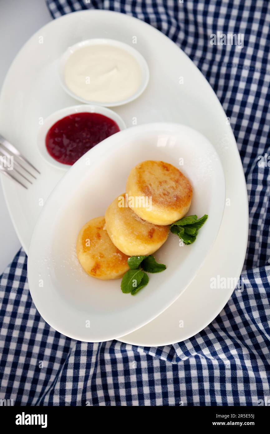Frittelle di formaggio ricotta rotonda in un piatto bianco su sfondo blu. Cibo prima colazione. Cibo sano. Salsa di panna acida e menta. Primo piano vista dall'alto. Pasto dessert. Frittelle di ricotta al formaggio ricotta. Foto Stock