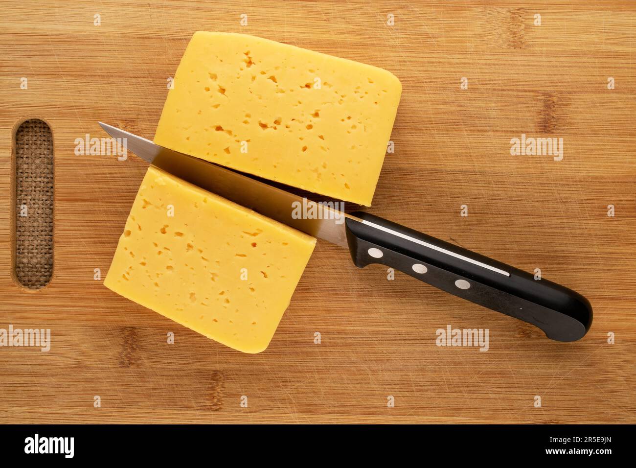 Tagliare il formaggio con un coltello su un tavolo da cucina in legno, macro, vista dall'alto. Foto Stock