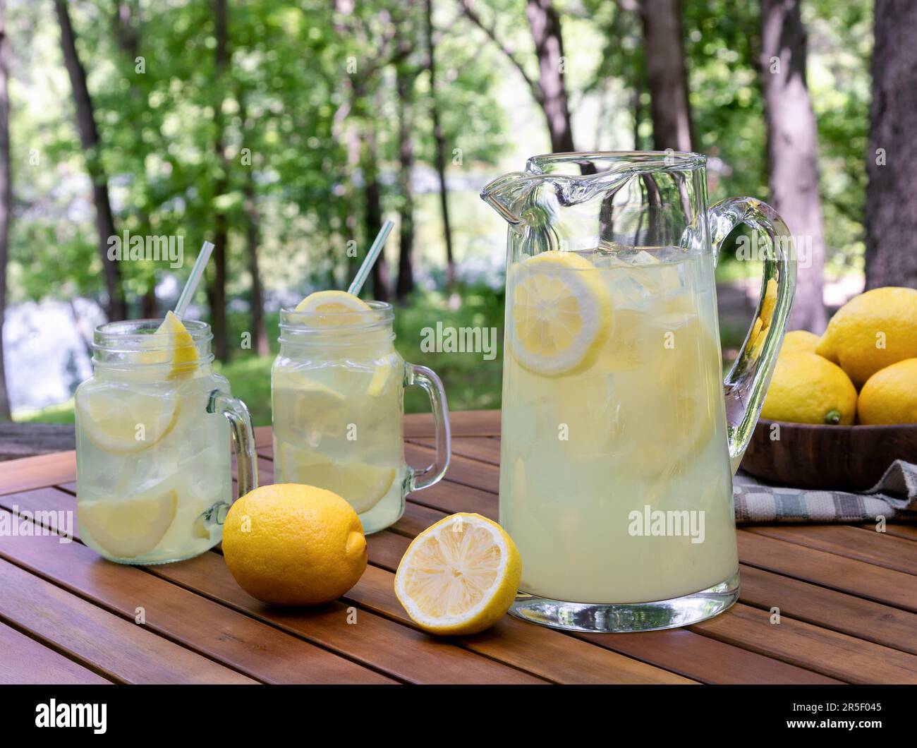 Caraffa di limonata con fettine di limone e ghiaccio all'aperto su un tavolo di legno con sfondo naturale Foto Stock