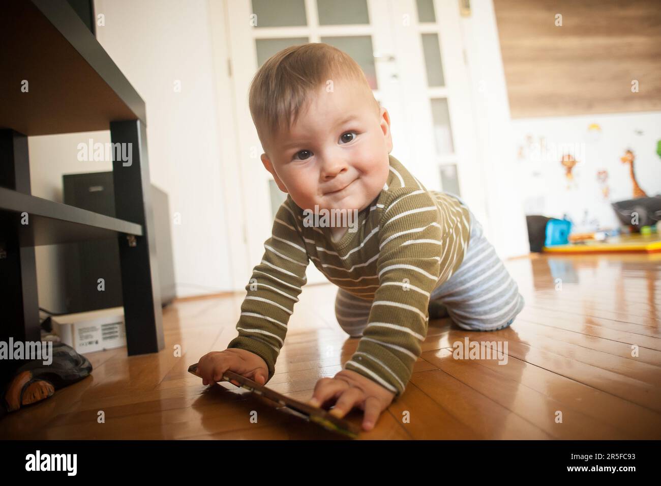 Il ritratto del ragazzo sorridente carino e sorridente striscia sul pavimento di casa e guarda la macchina fotografica. Concetto di gioia e felicità. Amore ed emozione familiare Foto Stock