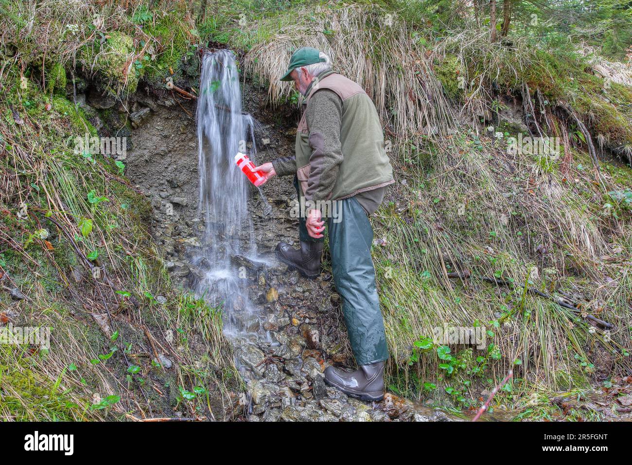 Dissetante trasparente per attività all'aperto. Un escursionista riempie la sua bottiglia di acqua potabile con le migliori acque cristalline di montagna. Foto Stock