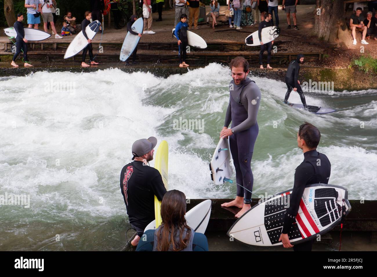 Surfisti all'onda artificiale di Eisbach sul fiume Isar che scorre attraverso il parco Englischer Garten (Giardini inglesi) a Monaco di Baviera in Germania Foto Stock