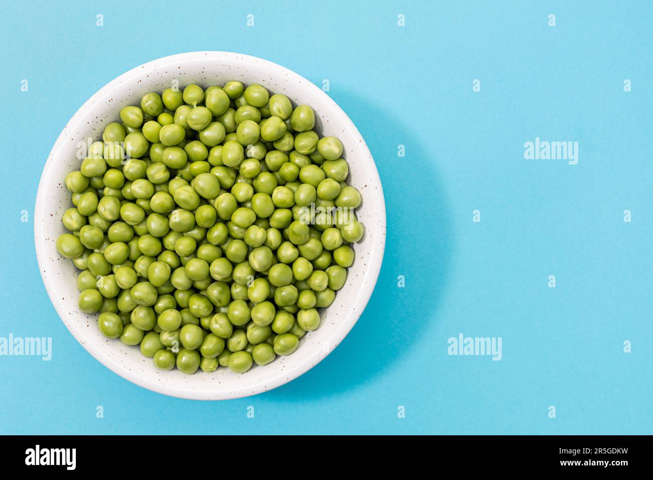 Piselli freschi verdi in ciotola isolato su fondo blu. Vista dall'alto. Spazio di copia Foto Stock