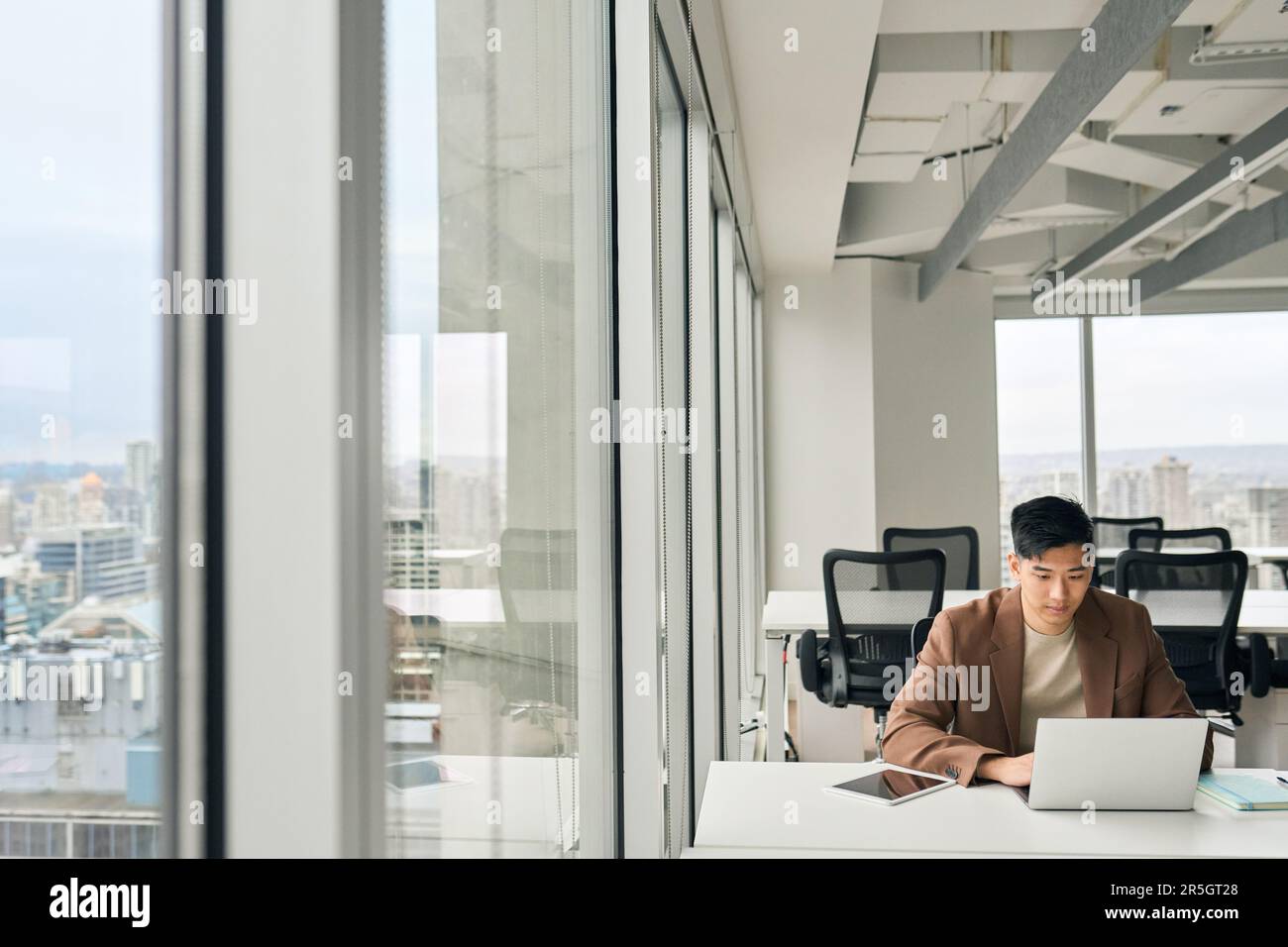 Giovane uomo d'affari asiatico che lavora su un computer portatile in un grande ufficio aziendale. Foto Stock