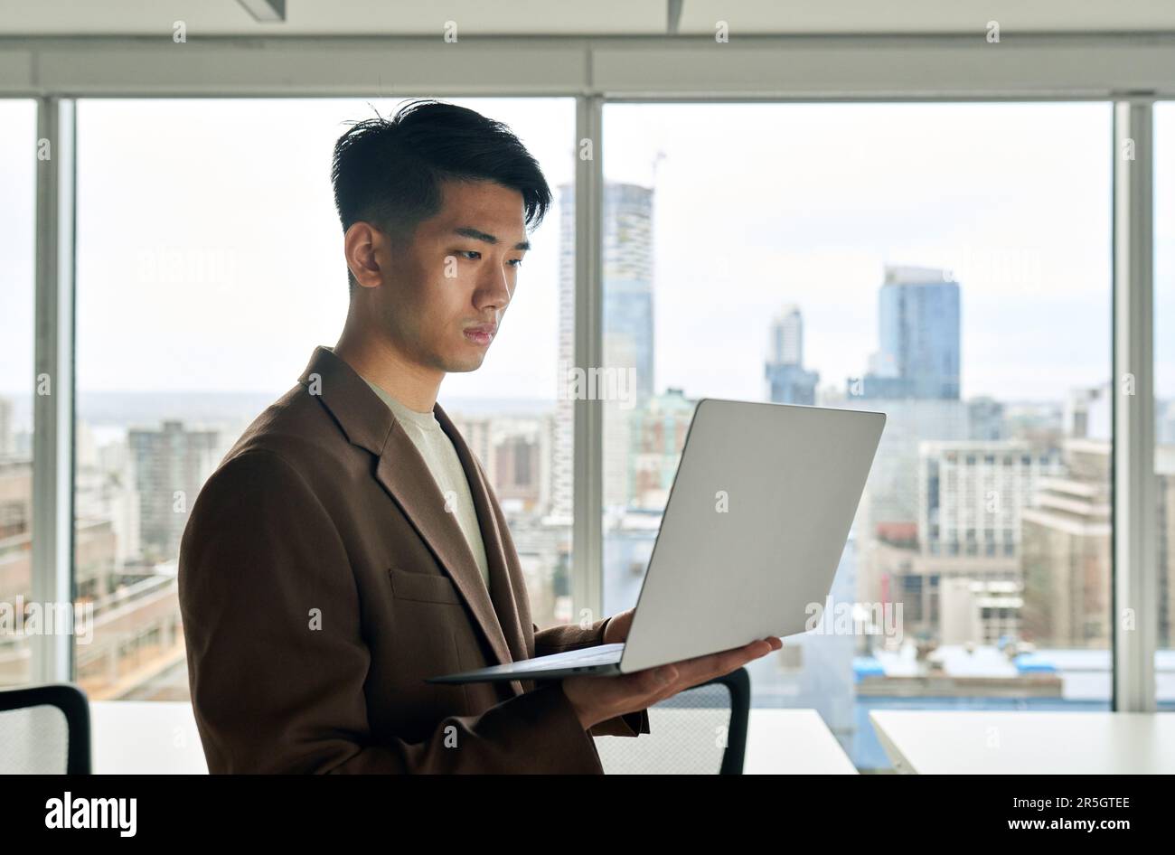 Giovane dipendente giapponese d'affari che tiene il portatile in piedi in un grande ufficio. Foto Stock