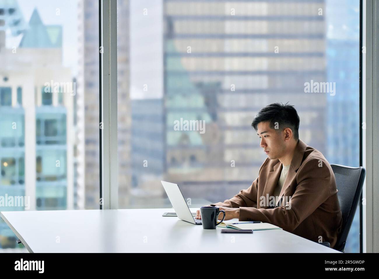 Giovane uomo d'affari asiatico serio che lavora su un computer portatile usando un computer in ufficio. Foto Stock
