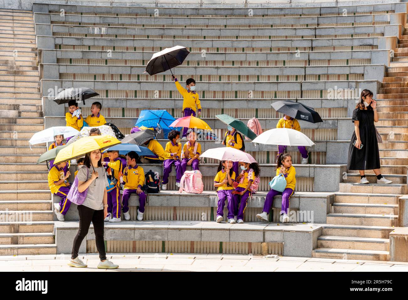 Un gruppo di scolari utilizza gli ombrelloni per Shelter from the Sun durante una visita all'Hong Kong Park, Hong Kong, Cina. Foto Stock