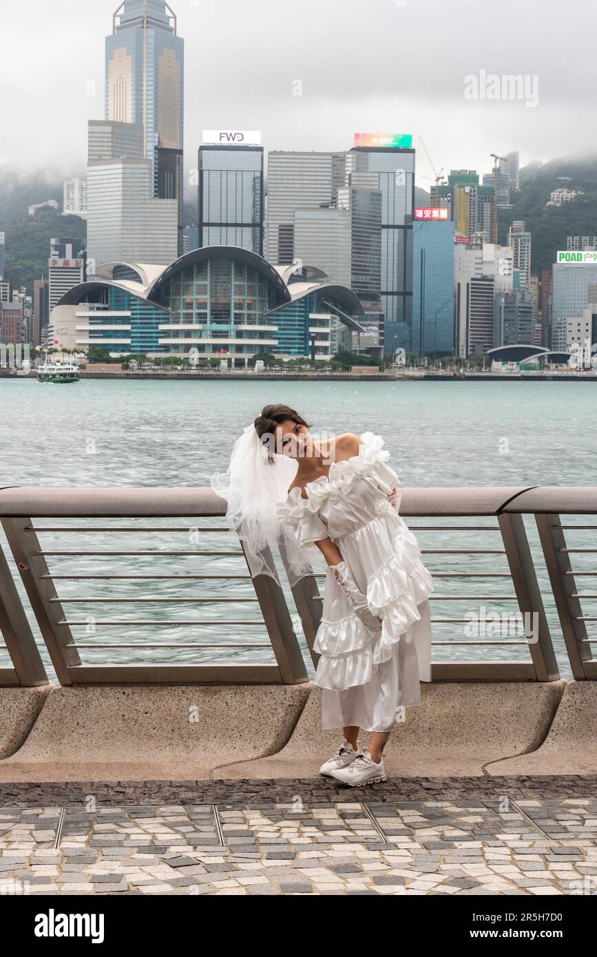 Una giovane donna in un vestito di nozze si prepara per le sue foto di nozze sul viale delle stelle con l'isola di Hong Kong come sfondo, Kowloon, Hong Kong. Foto Stock