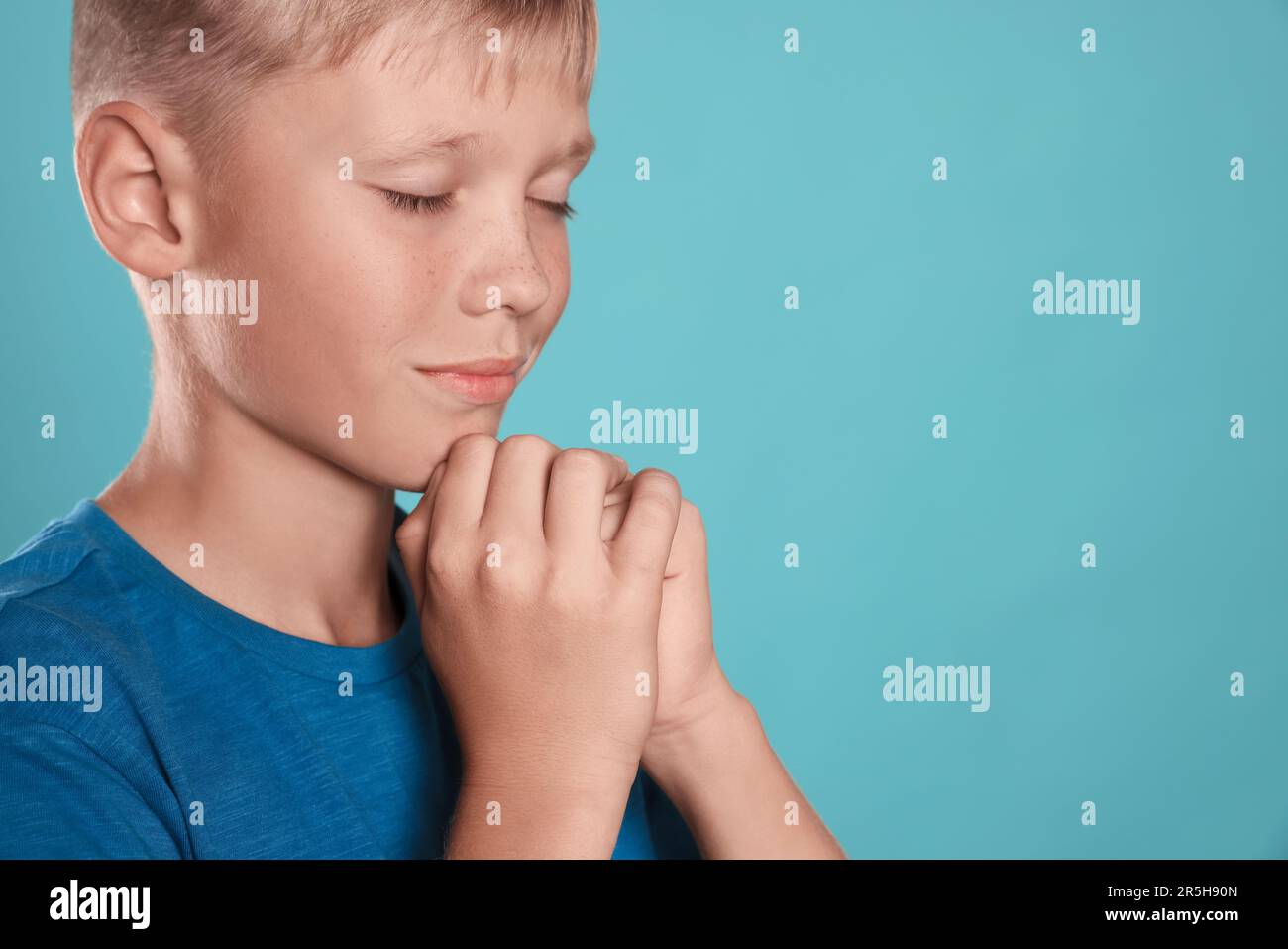 Ragazzo con mani stringate che prega su fondo turchese, primo piano. Spazio per il testo Foto Stock