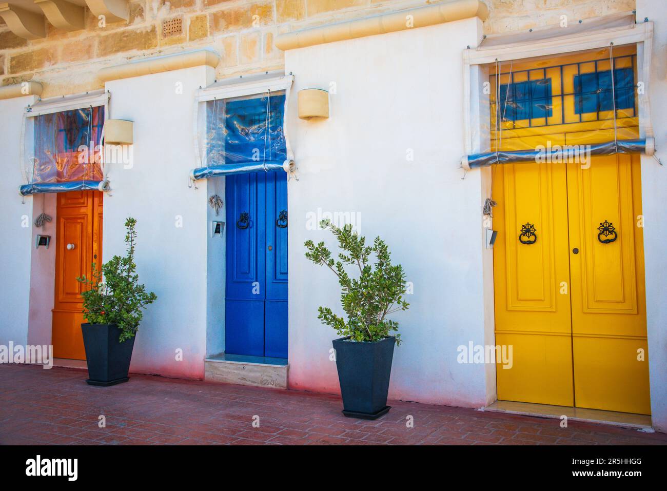 Tre porte colorate arancione blu giallo con piante in vaso Foto Stock