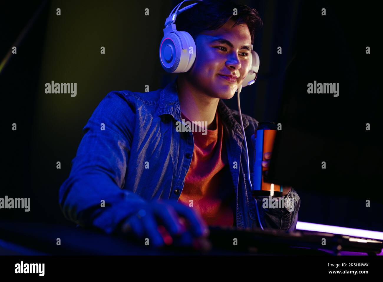 Concentrato e determinato, un giocatore di computer tiene la sua bevanda energetica in una mano mentre guarda lo schermo. Giocatore che alimenta la sua energia con una bevanda, k Foto Stock