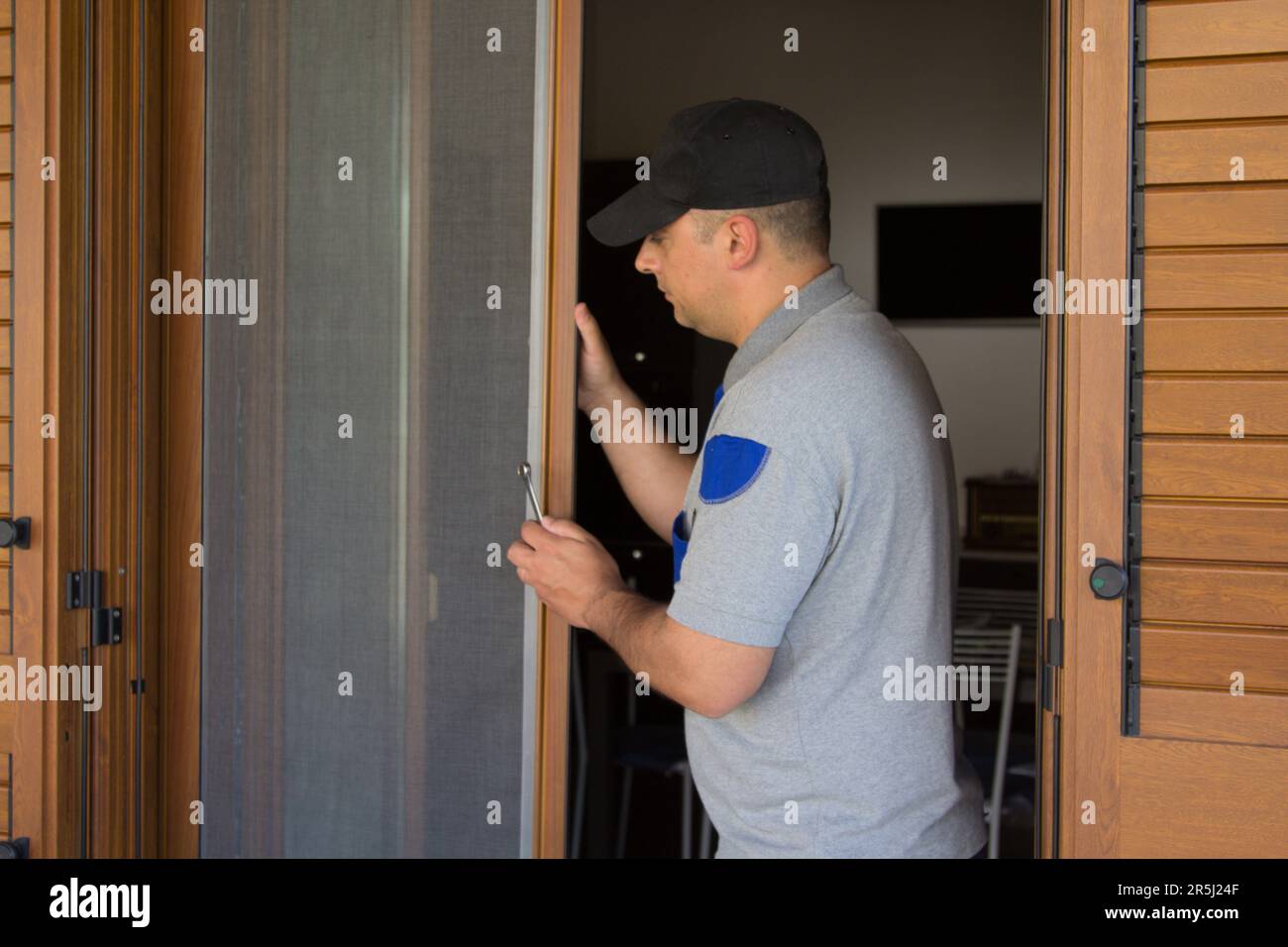 Immagine di un handyman che installa uno schermo del mosca in una finestra francese della sua casa. Protezione della casa da insetti. Foto Stock