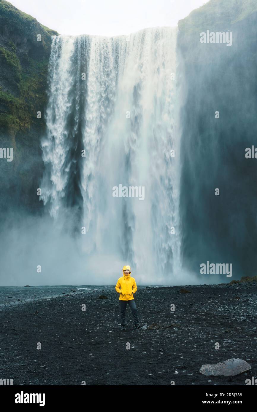 Scenografico scenario della cascata di Skogafoss che scorre con una donna asiatica in piedi in estate in Islanda Foto Stock