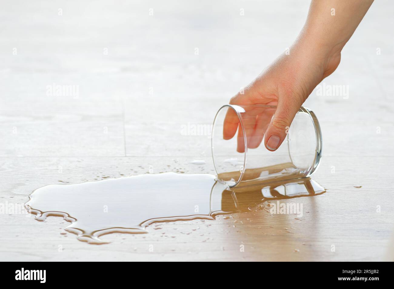 Primo piano di una mano che tiene un bicchiere d'acqua da un pavimento in legno laminato Foto Stock