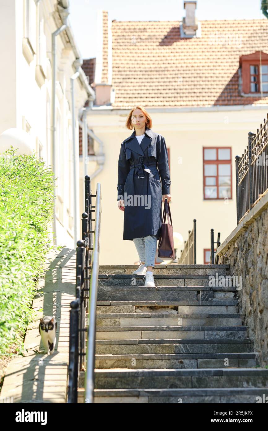 Donna rossa in trench blu e sneakers che scendono le scale Foto Stock