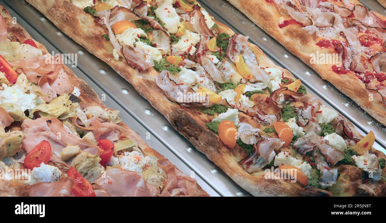 Molte focaccie chiamate anche pinsa romana in Italia con mozzarella e affettati e verdure miste in vendita in pizzeria Foto Stock