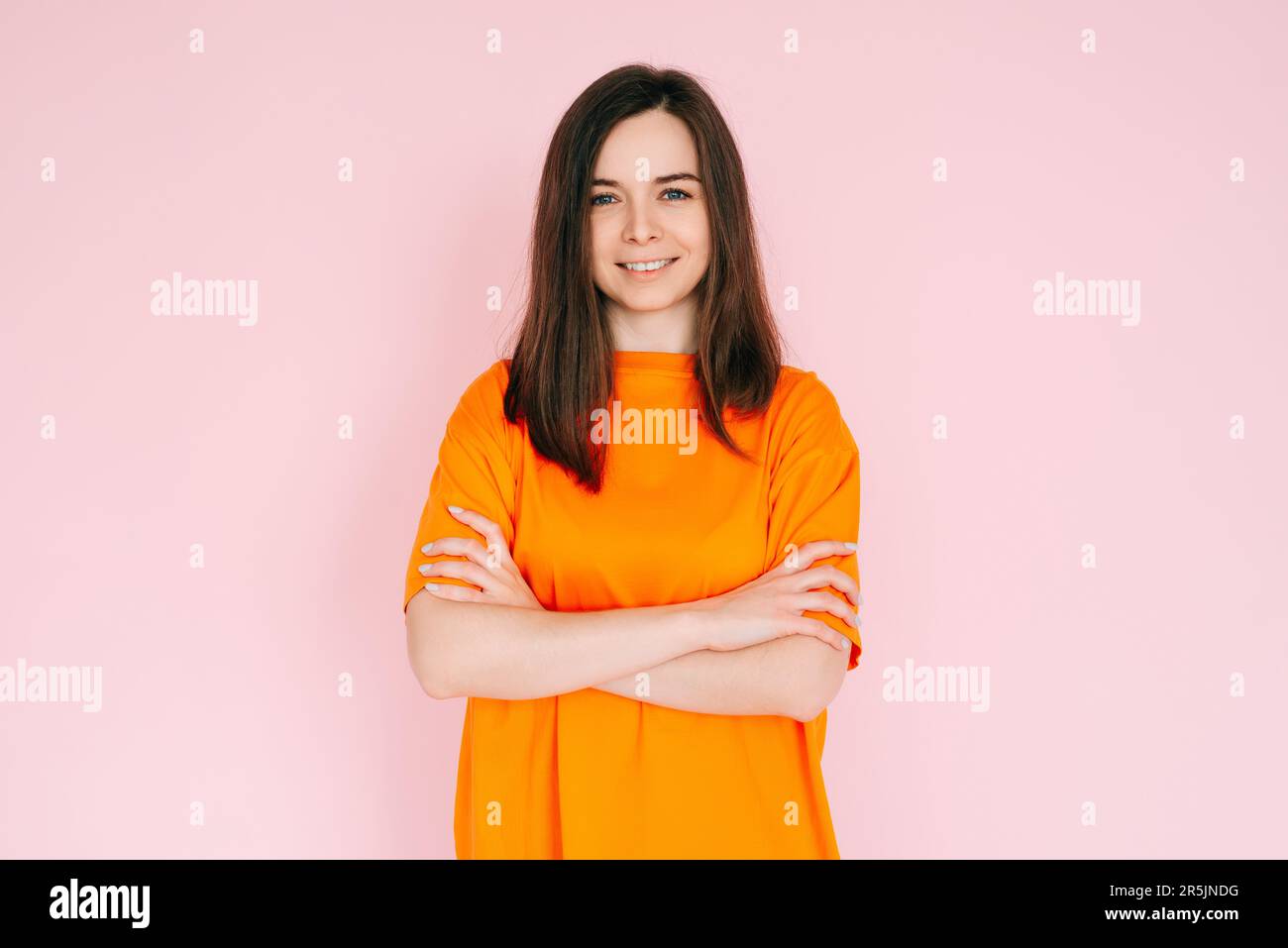 Gioia radiante: Donna bella con il sorriso e le braccia che si incrociano, abbracciando il buon umore in abbigliamento comodo - positività vibrante su sfondo rosa. Foto Stock