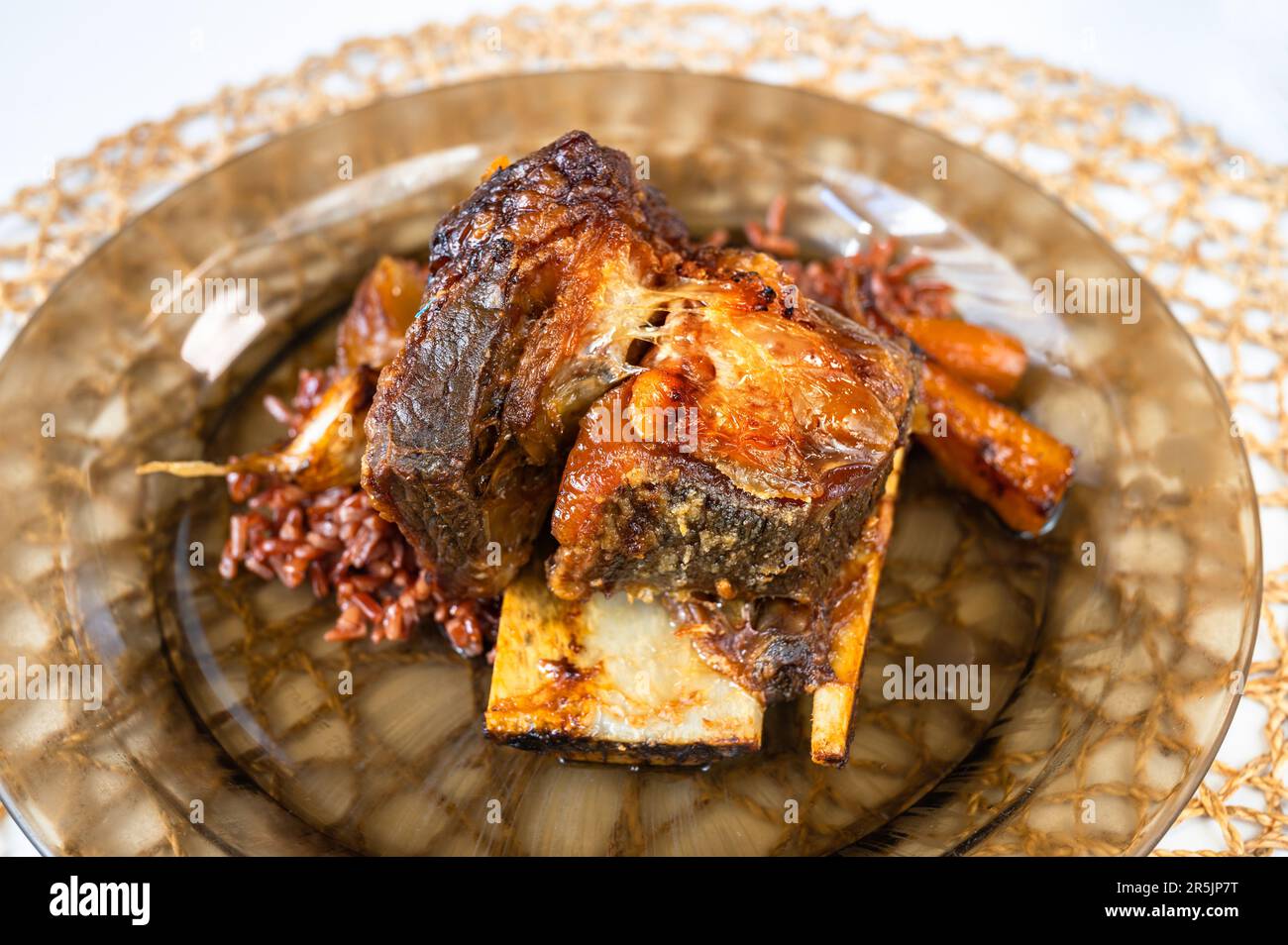 Costolette di manzo al forno con riso rosso su piatto marrone su cialda di bambù circolare, primo piano. Foto Stock