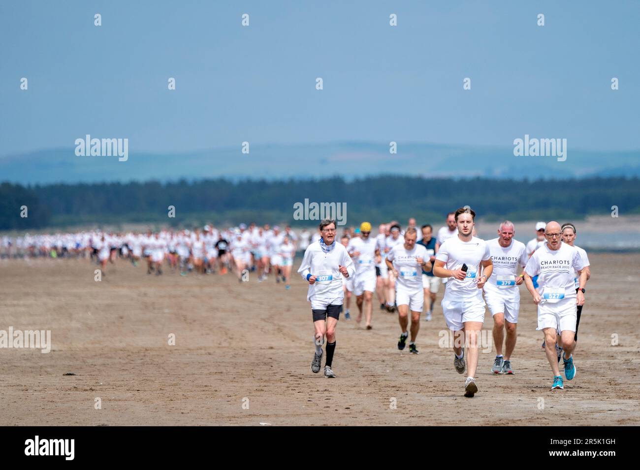 I corridori, che indossano il bianco, gareggiano nella gara annuale dei carri di fuoco lungo la West Sands Beach a St Andrews, Fife. La gara del 5km prende parte nello stesso luogo in cui è stata girata la famosa scena di corsa del film del 1981 carri di fuoco. I proventi dell'evento sono donati all'RNLI e alle associazioni di beneficenza locali. Data immagine: Domenica 4 giugno 2023. Foto Stock