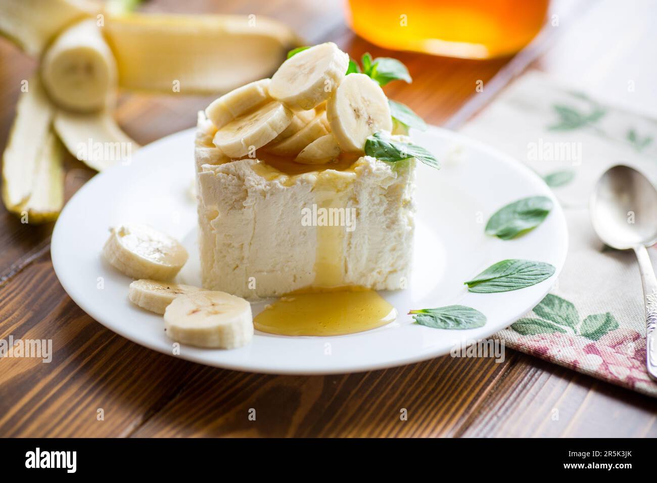 Porzione di cagliata di latte fatta in casa con fette di banana e miele, con menta in un piatto. Foto Stock