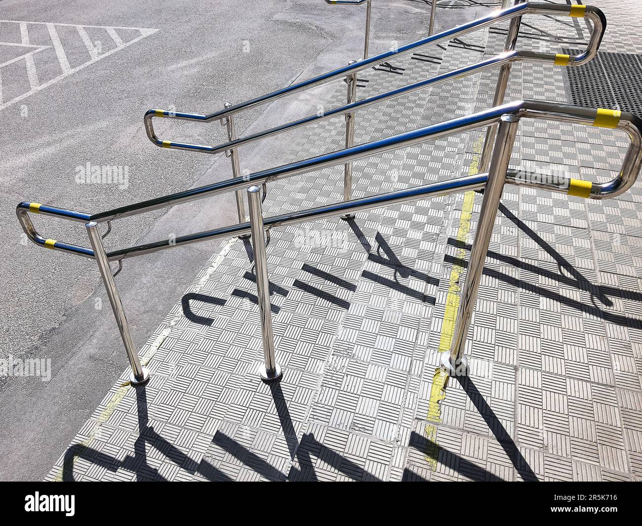 Simbolo dei disabili nel parcheggio con passaggio per disabili, persone che spingono passeggini, carrelli con barre in acciaio inox per evitare cadute. Foto Stock