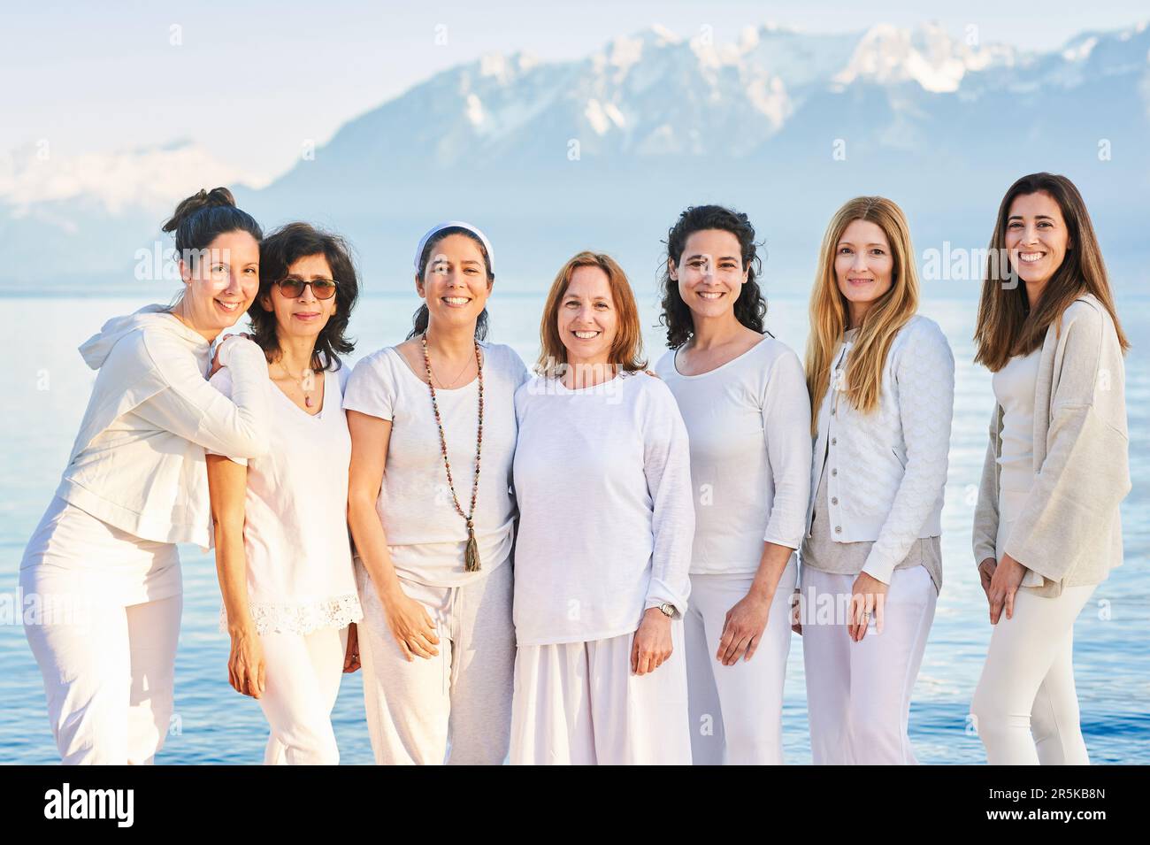 Ritratto di gruppo di belle donne che si posano all'esterno con un bellissimo paesaggio montano sullo sfondo, indossando abiti bianchi Foto Stock