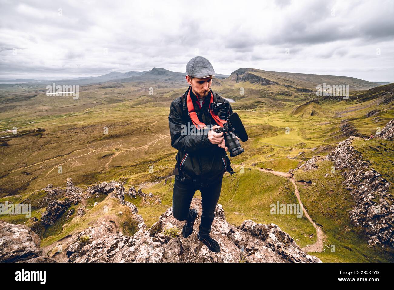 In un punto panoramico mozzafiato a Quiraing, Scozia, un fotografo colpisce una posa, aggrappando telecamere come strumenti del loro mestiere. Sullo sfondo Foto Stock