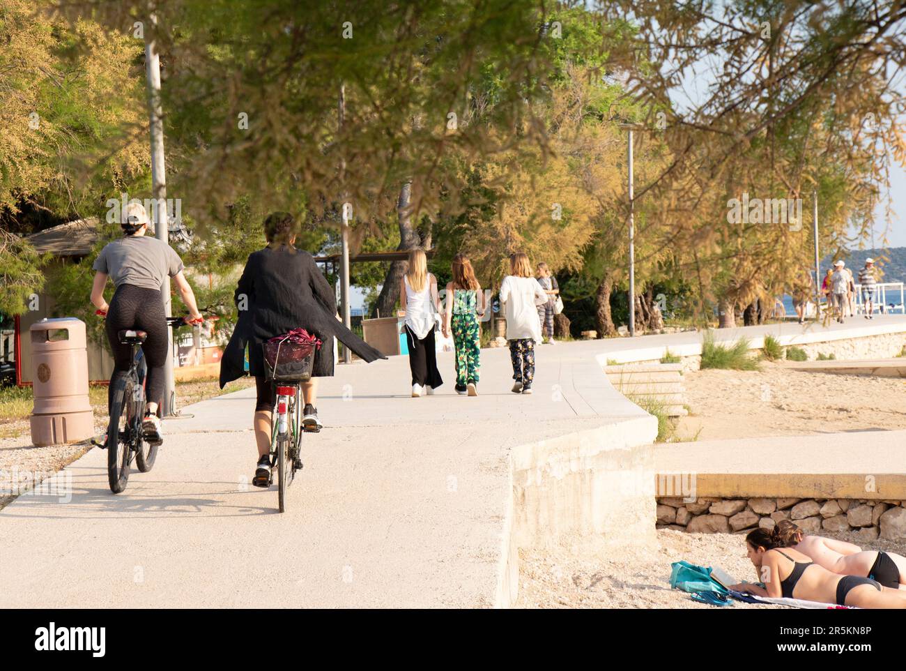 Vodice, Croazia - 27 maggio 2023: Passeggiata con pini al mare e persone a piedi, in bicicletta o al sole Foto Stock