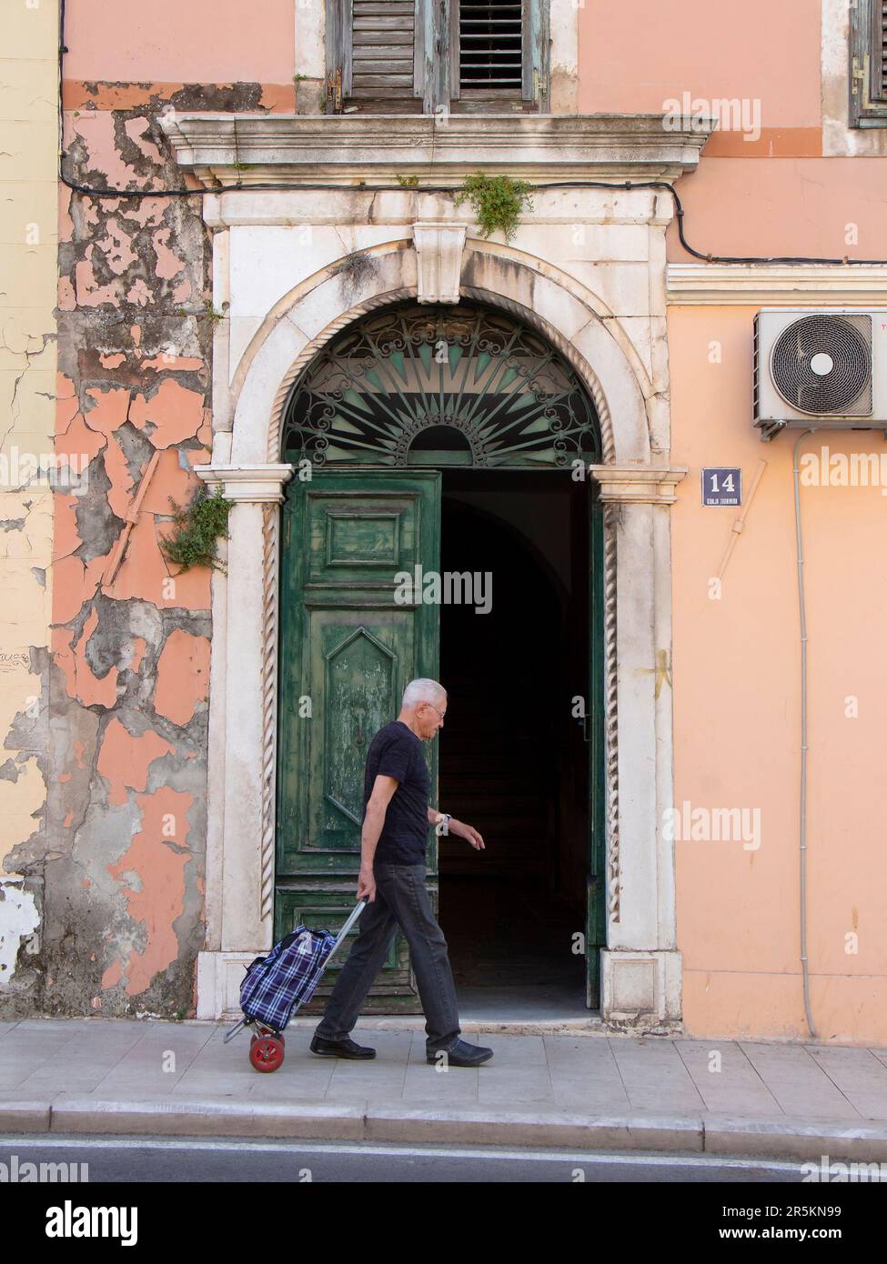 Sibenik, Croazia - 31 maggio 2023: Un uomo anziano che cammina dalla porta d'ingresso dell'arco mentre tira il carrello Foto Stock