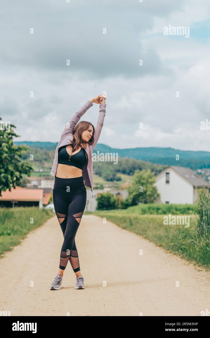 Ritratto all'aperto di giovane donna bella vestibilità con abbigliamento sportivo nero, stretching modello atleta, moda sportiva Foto Stock