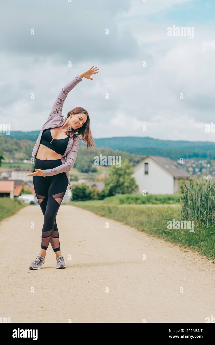 Ritratto all'aperto di giovane donna bella vestibilità con abbigliamento sportivo nero, stretching modello atleta, moda sportiva Foto Stock