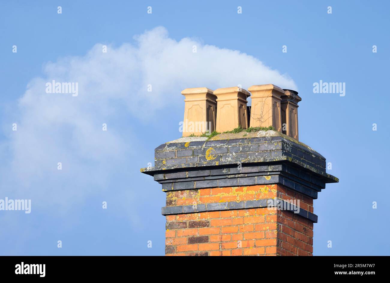 Fumo di legno contro un cielo blu che splendente da un camino di mattoni di una vecchia casa del Regno Unito Foto Stock