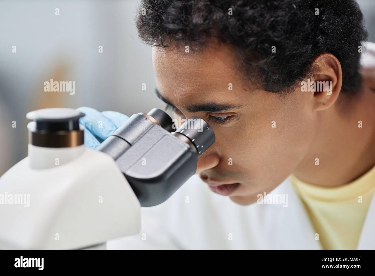 Primo piano dell'uomo etnico come scienziato che guarda al microscopio mentre fa ricerca in laboratorio, copia spazio Foto Stock