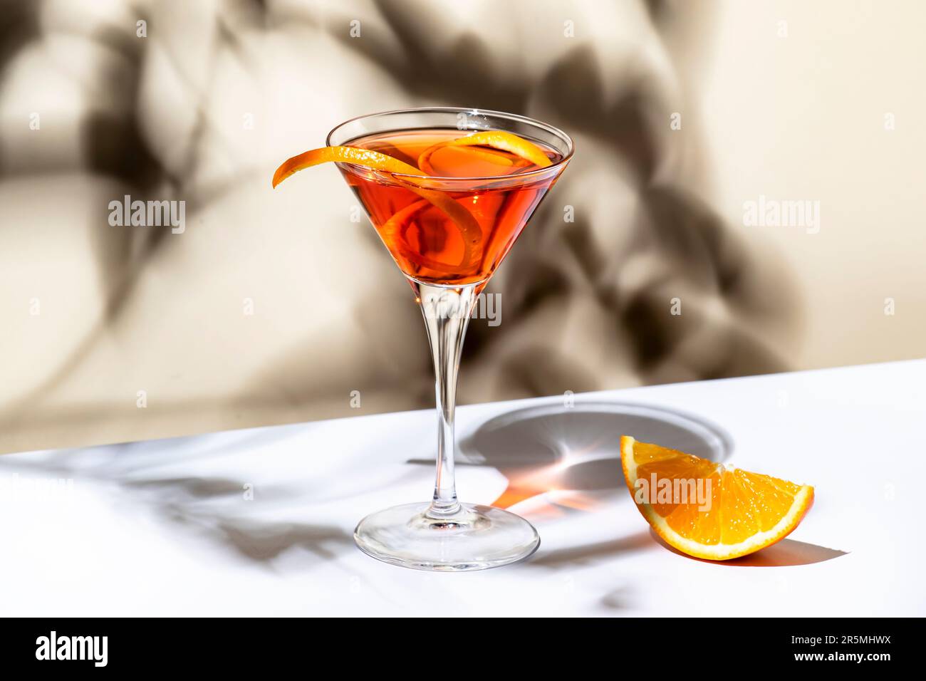 Cocktail d'arancia Martinez con vermouth rosso, liquore, amaro, scorza di  agrumi e ghiaccio in bicchiere martini. Sfondo beige chiaro, luce forte,  ombra pa Foto stock - Alamy