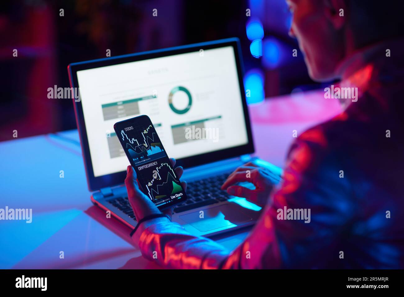 Visto da dietro moderna donna d'affari con laptop e smartphone che commerciano criptovalute in un ufficio moderno. Foto Stock
