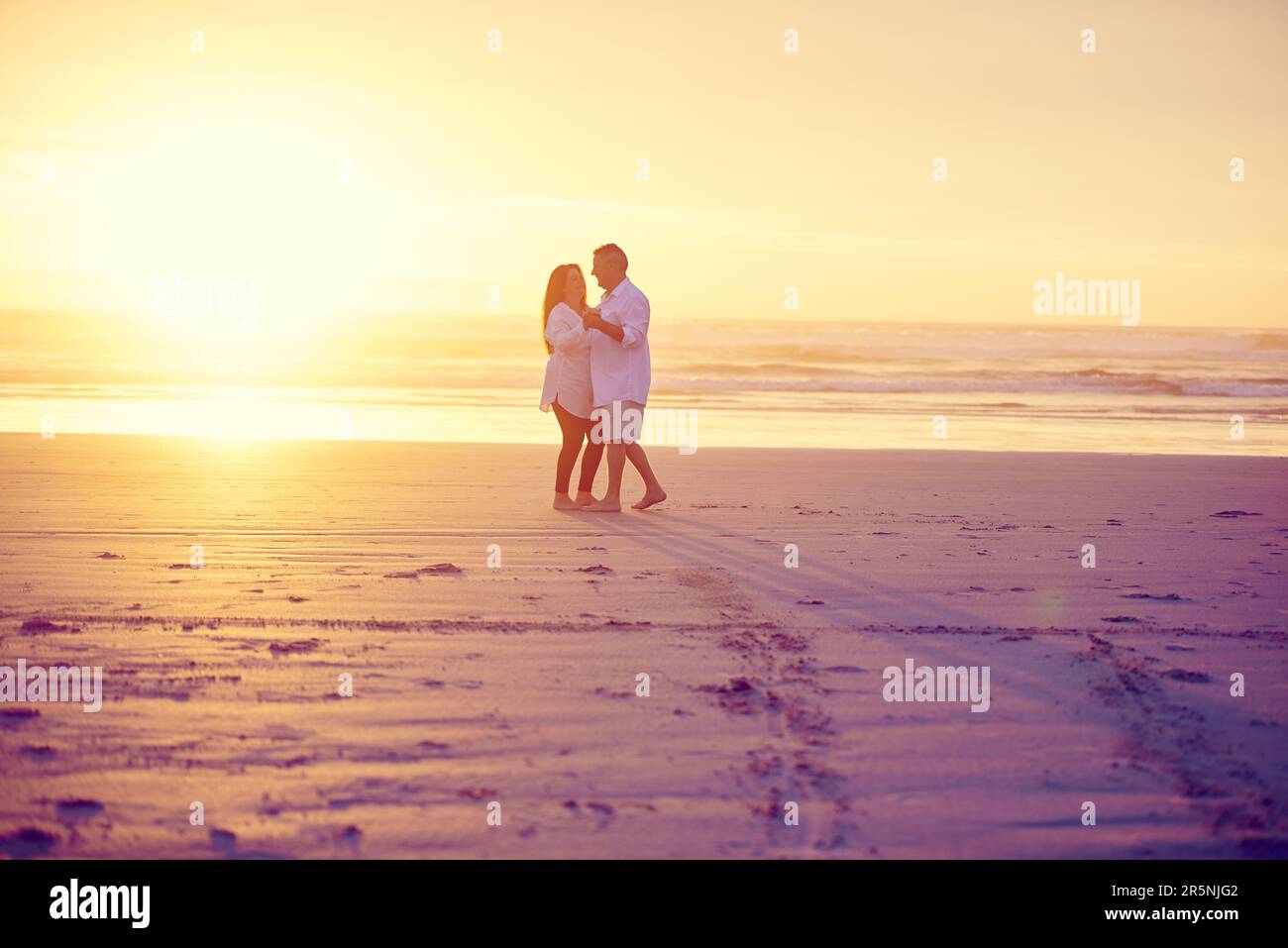 Balli lenti nella sabbia. Scatto completo di una coppia matura affettuosa che ballerà sulla spiaggia al tramonto. Foto Stock