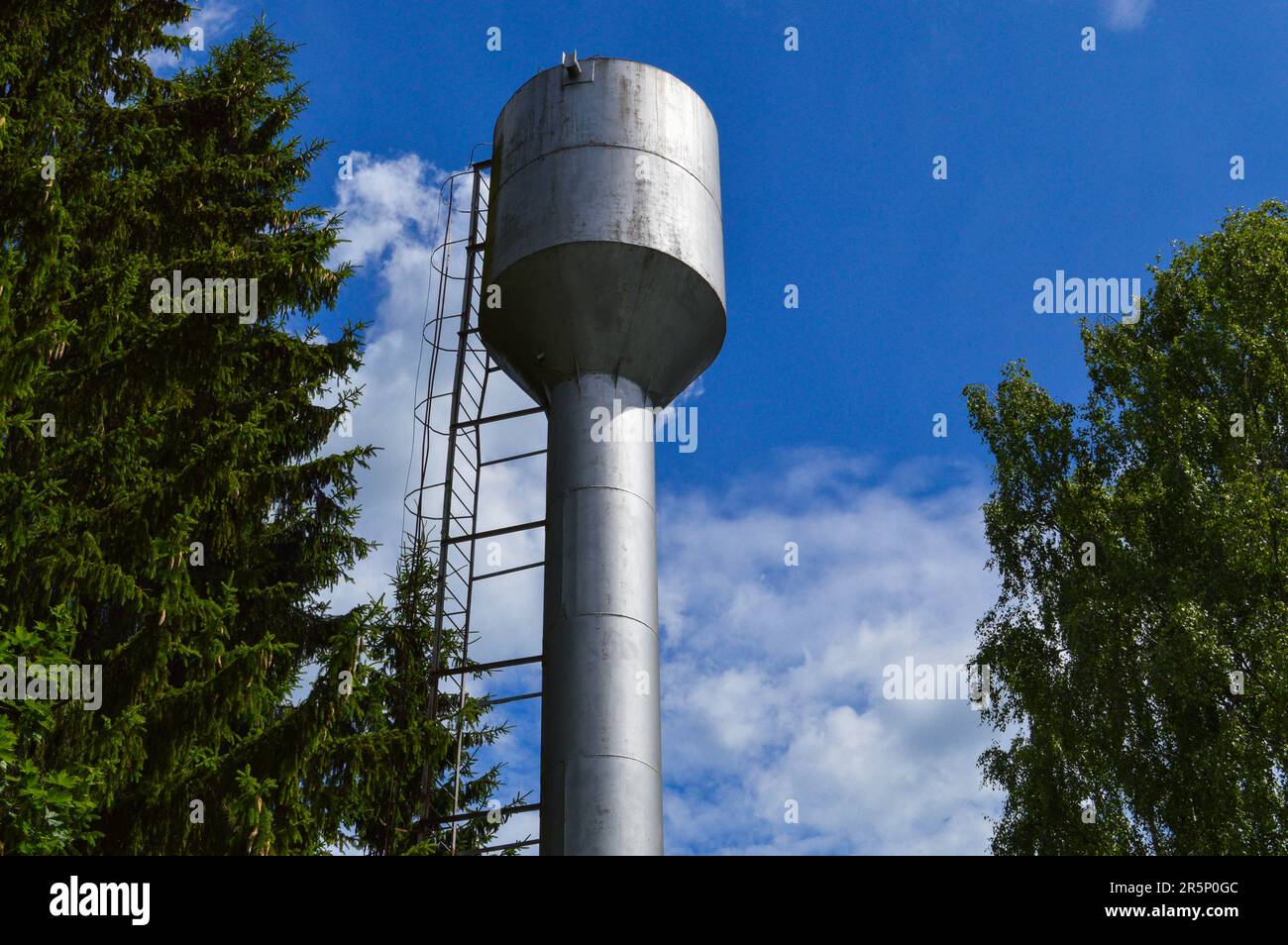 Grande torre dell'acqua industriale in acciaio inossidabile lucido per l'approvvigionamento di acqua di grande capacità, barile contro il cielo blu e gli alberi. Foto Stock