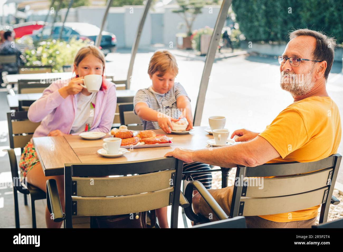 Famiglia con bambini che fanno colazione in un bar o in un ristorante all'aperto, bevendo cioccolata calda, mangiando panetterie Foto Stock