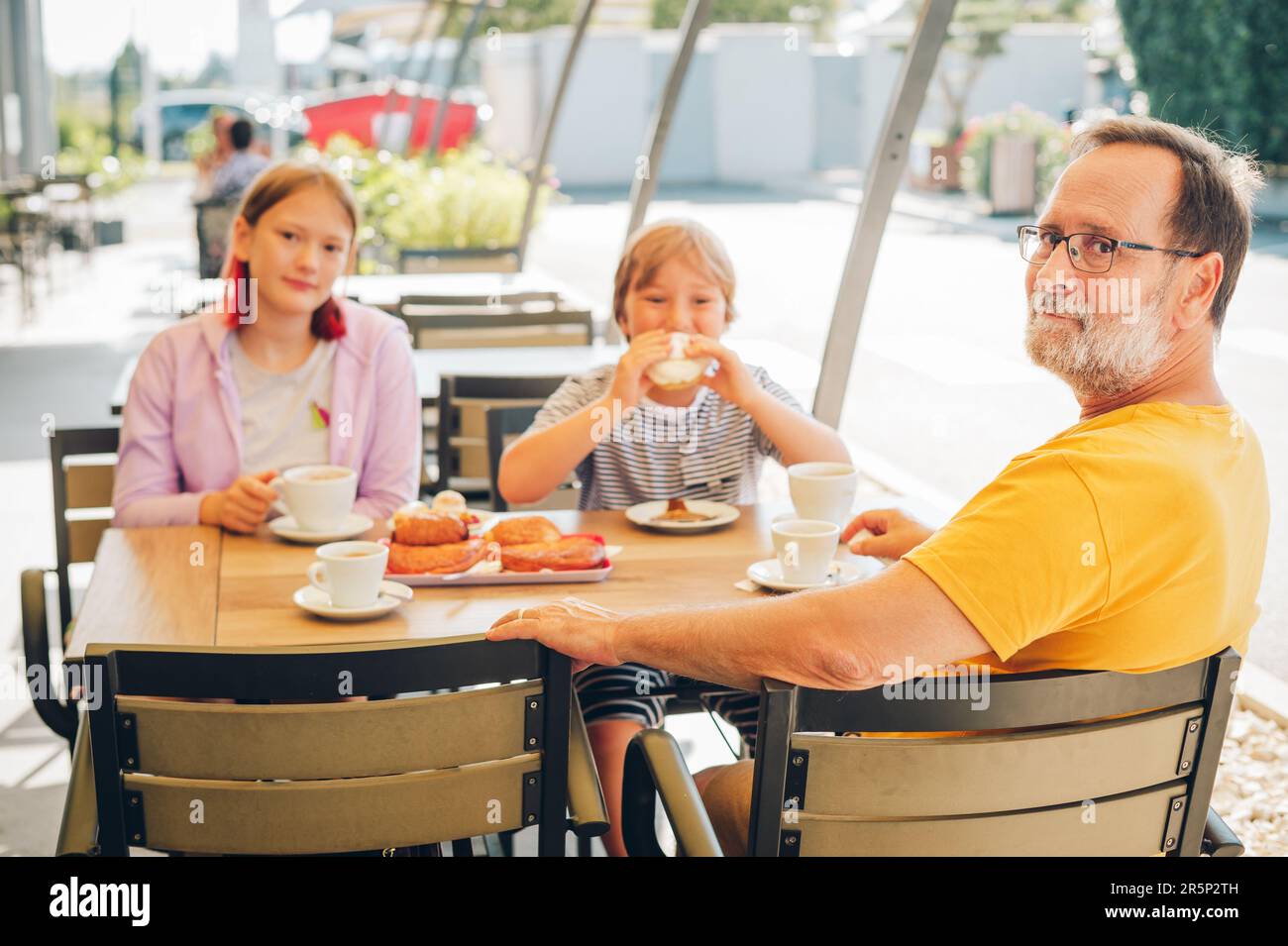 Famiglia con bambini che fanno colazione in un bar o in un ristorante all'aperto, bevendo cioccolata calda, mangiando panetterie Foto Stock
