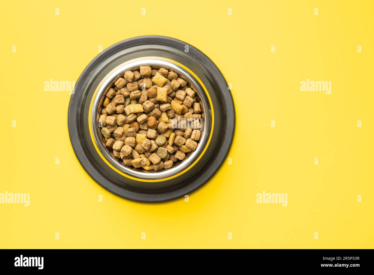 Pappe per animali domestici a secco. Cibo per cani o gatti in ciotola su sfondo giallo. Vista dall'alto. Foto Stock