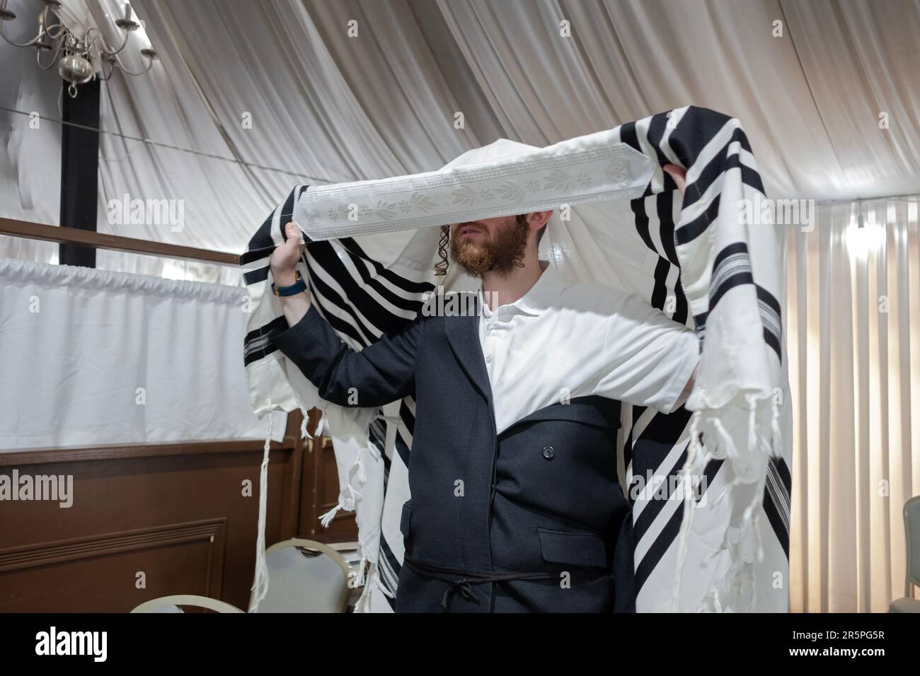 Prima dei servizi mattutini e mentre si mette su un suo tallis, un uomo ebraico ortodosso si impegna in un momento di contemplazione. In una sinagoga di Monsey, NY. Foto Stock