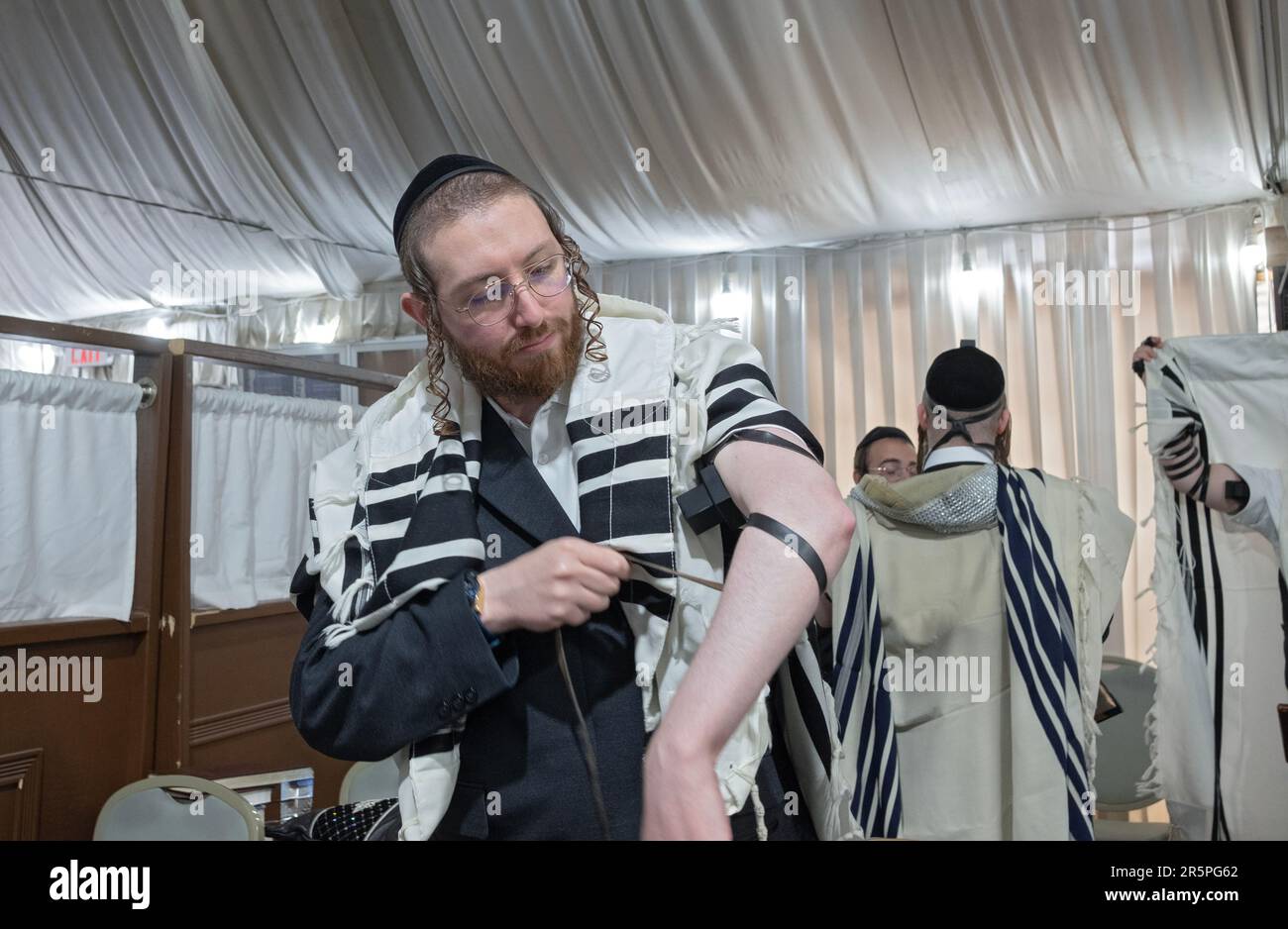 Un uomo ebraico ortodosso si mette in tefillin prima delle preghiere del mattino. In una sinagoga a Monsey, New York. Foto Stock